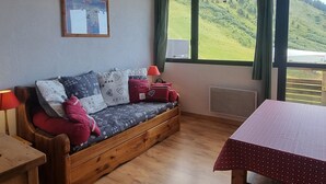 Een gezellige kamer met een houten bank, een tafel en een groot raam met uitzicht op een groen landschap.