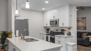 A modern kitchen with white cabinetry, a stainless steel sink, a built-in oven, and a microwave. There is a small island with a sink and a trash can. - Chic Uptown Condo Tucson (Tucson)
