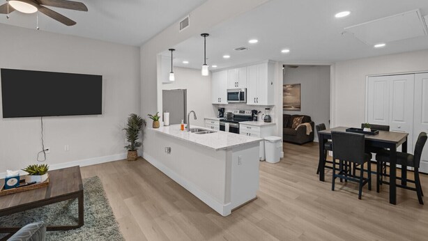 A modern kitchen with white cabinetry, a central island, and a dining area with a table and chairs. - Chic Uptown Condo Tucson (Tucson)