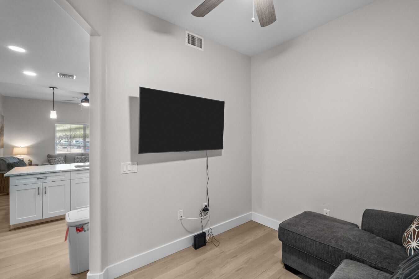 A modern living room with a flat-screen TV mounted on the wall, a grey sofa, and a wooden floor.
