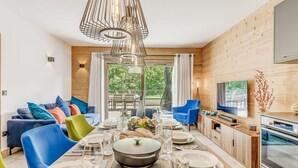 Un espace repas moderne avec une table en bois dressée pour le repas, un canapé agrémenté de coussins colorés et un téléviseur fixé au mur.