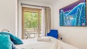 Une chambre d’hôtel avec un lit, une chaise bleue, un tableau et un balcon aménagé avec du mobilier d’extérieur.