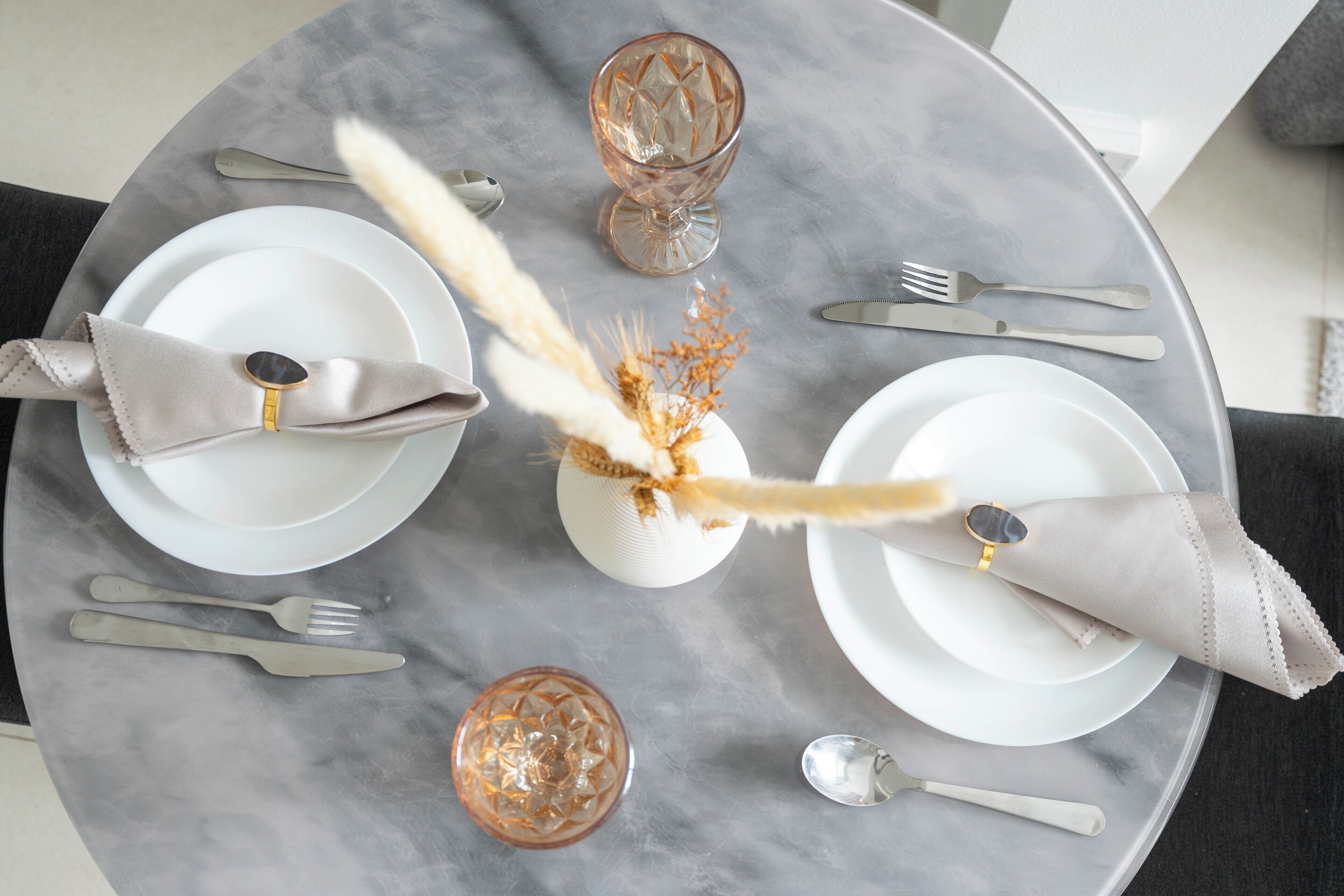 Une table ronde surmontée d’un plateau en marbre, dressée avec de l’assiette blanche, des couverts en argent et de la verrerie décorative.
