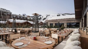 An outdoor dining area with round wooden tables and chairs, set against a backdrop of snow-covered mountains and a clear sky. - Luxury apartment in the heart of Courchevel 1850 (Courchevel 1850)