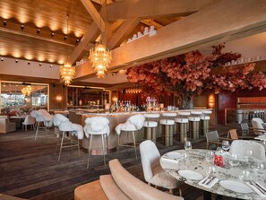 A restaurant with a bar area, wooden ceiling, and white fur-covered chairs.