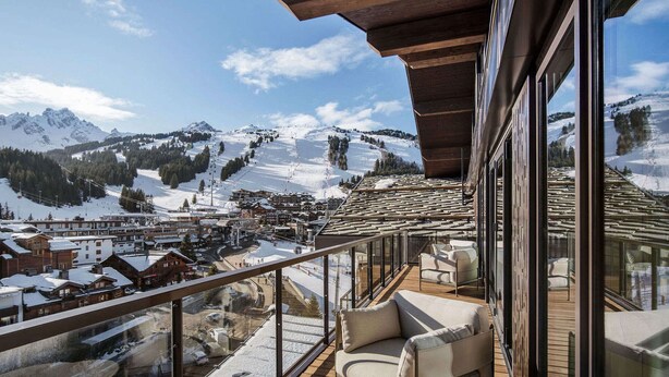 Un balcon offrant une vue sur une ville de montagne enneigée, avec une terrasse en bois et un espace salon.