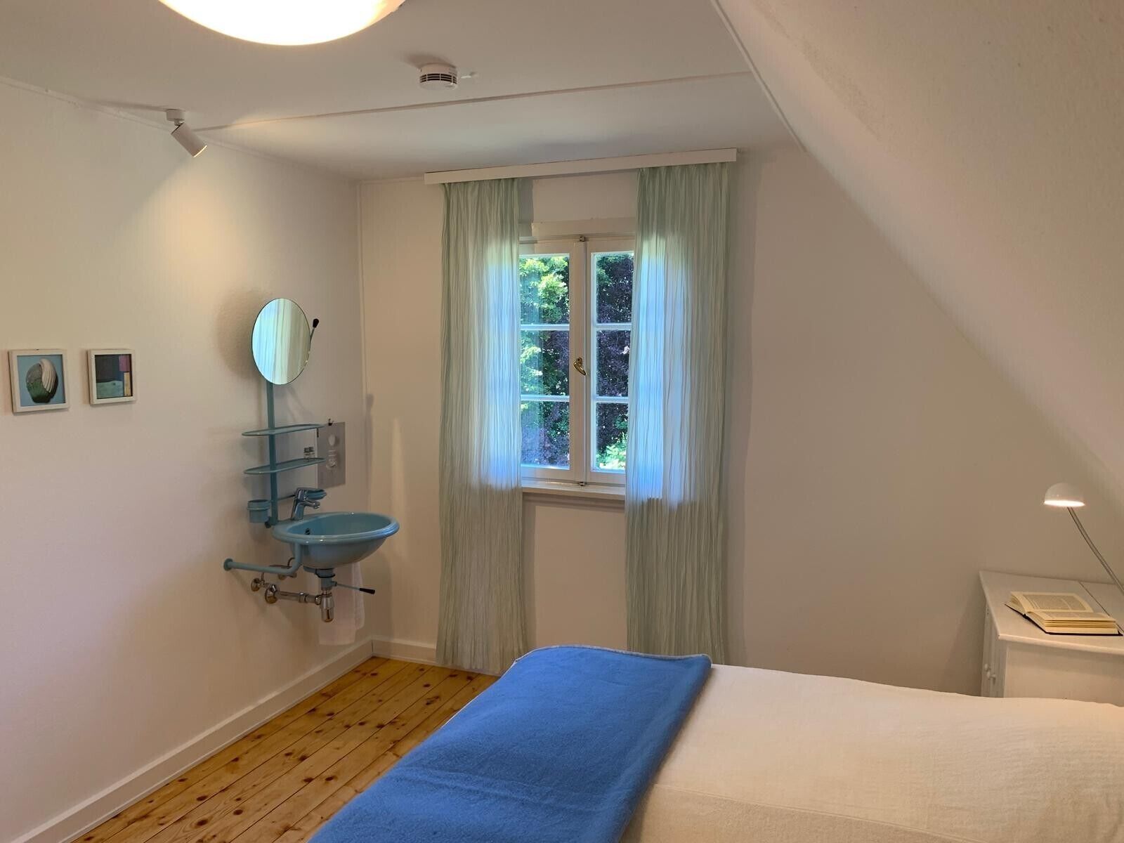 Une chambre à coucher avec un lit, une fenêtre avec des rideaux, un lavabo et un miroir.