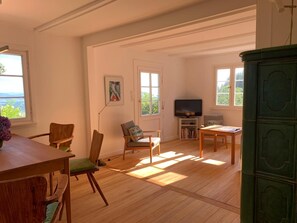 A spacious living room with a wooden floor, a television, a sofa, and a dining area with chairs.