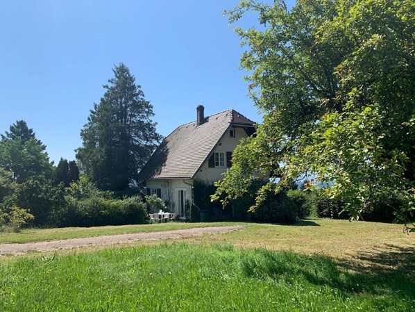 A house with a sloped roof, surrounded by greenery and trees.