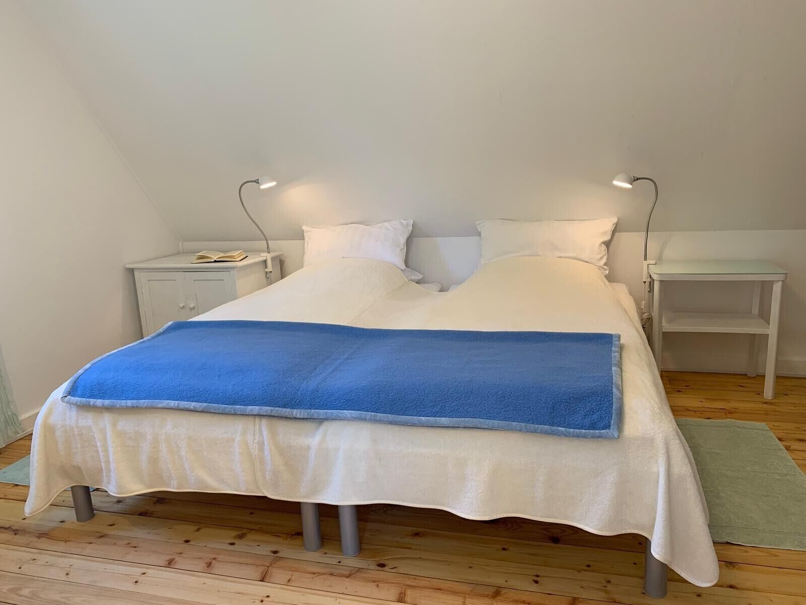 Una cama con un edredón azul, almohadas blancas y dos mesitas de noche con lámparas.