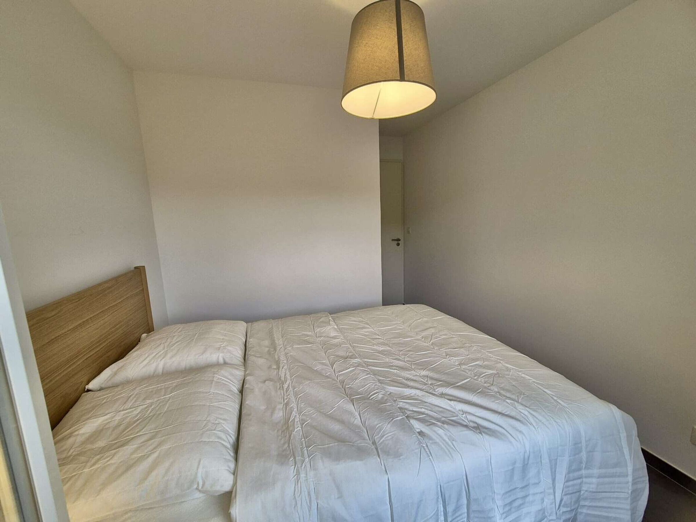 Uma cama de solteiro com cabeceira de madeira em um quarto com paredes brancas e um lustre.
