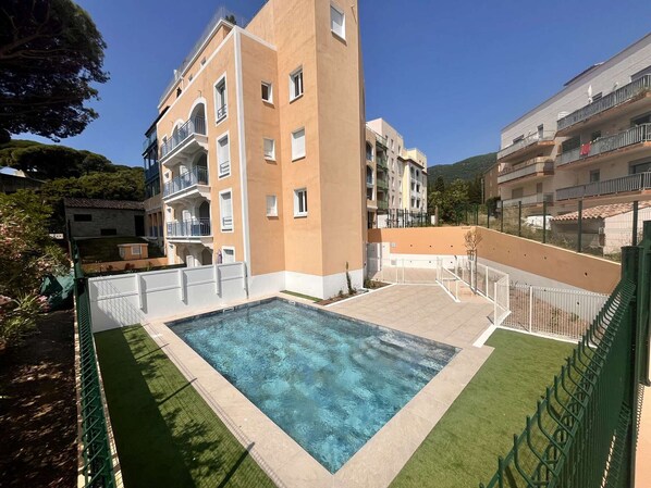 A swimming pool surrounded by apartment buildings with balconies, a clear sky, and a mountainous background. - Modern apartment with pool, air conditioning, and parking in Cavalaire-sur-Mer (Cavalaire-sur-Mer)