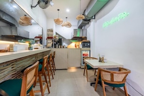 A modern kitchen with a bar area, wooden chairs, and a neon sign. - Bali Bay By Urban Haven (Denpasar)