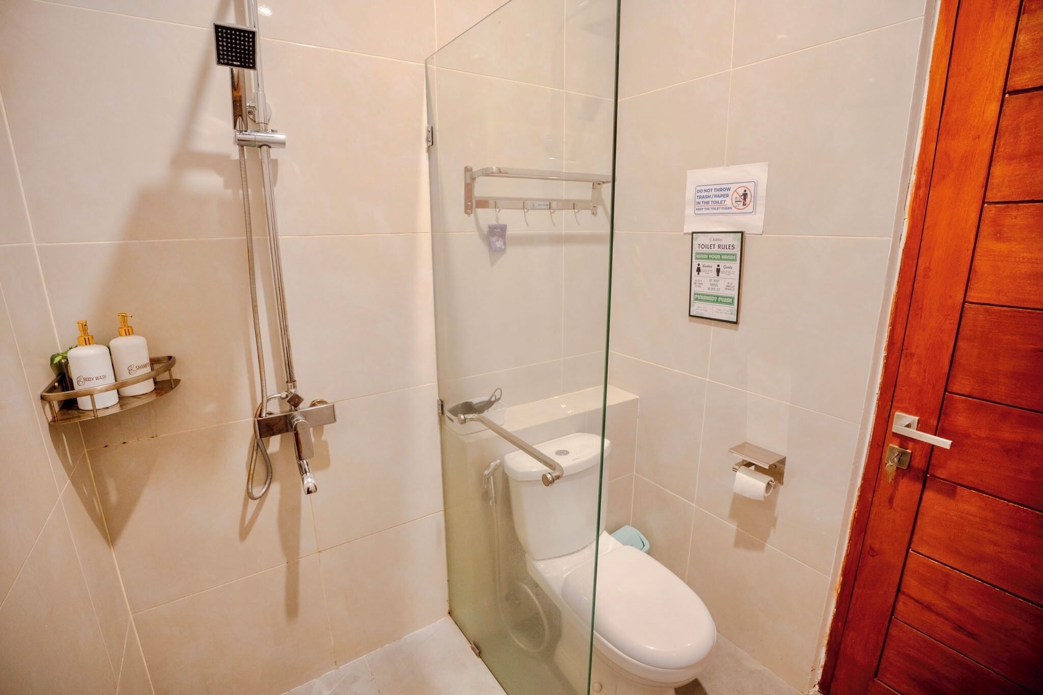 Un baño con ducha de vidrio, inodoro y puerta de madera.