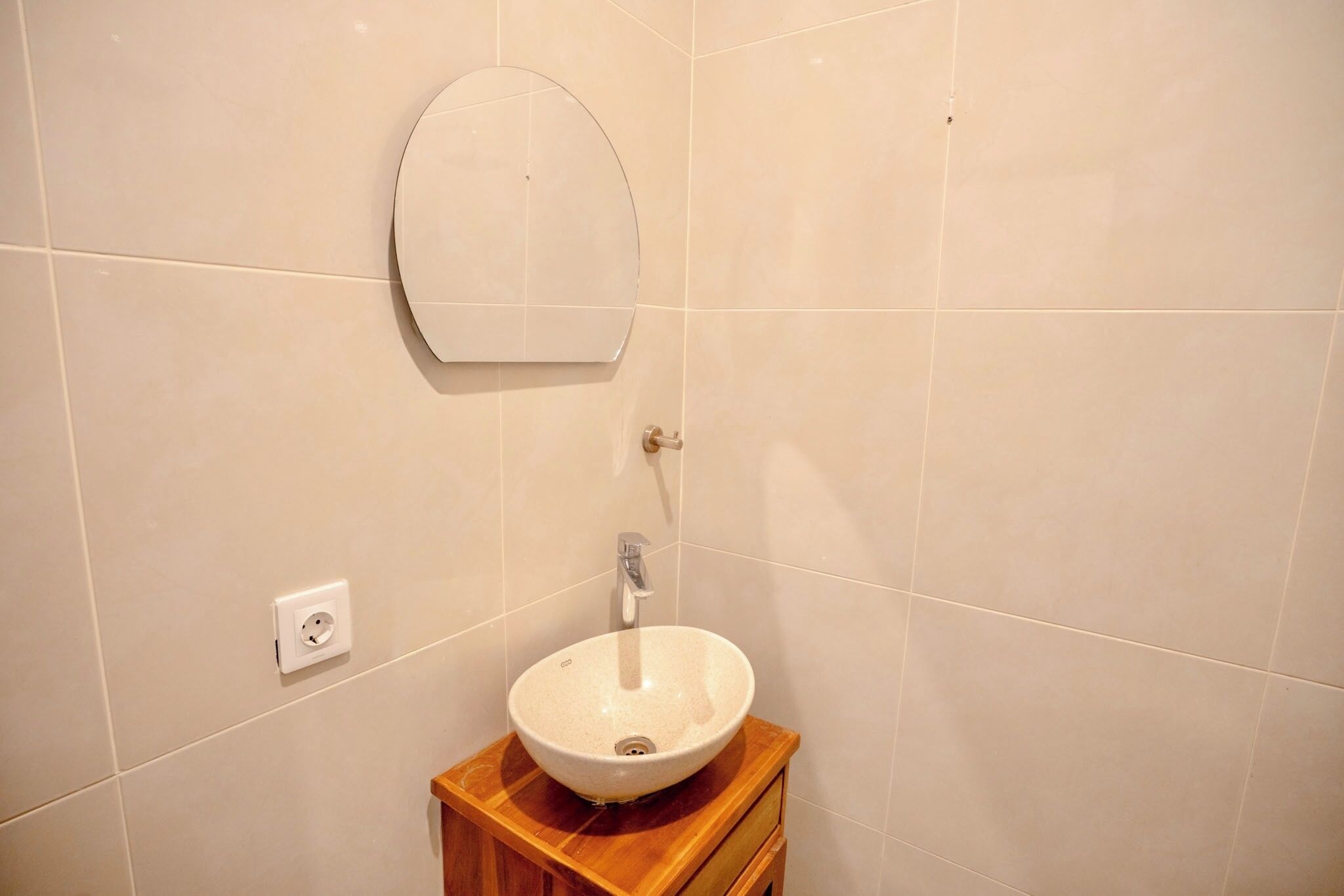 A bathroom with a round mirror, a sink, and a wooden vanity.