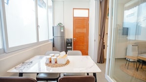 A modern dining area with a marble table, chairs, a refrigerator, and a sliding glass door leading to a balcony. - Bali Bay By Urban Haven (Denpasar)