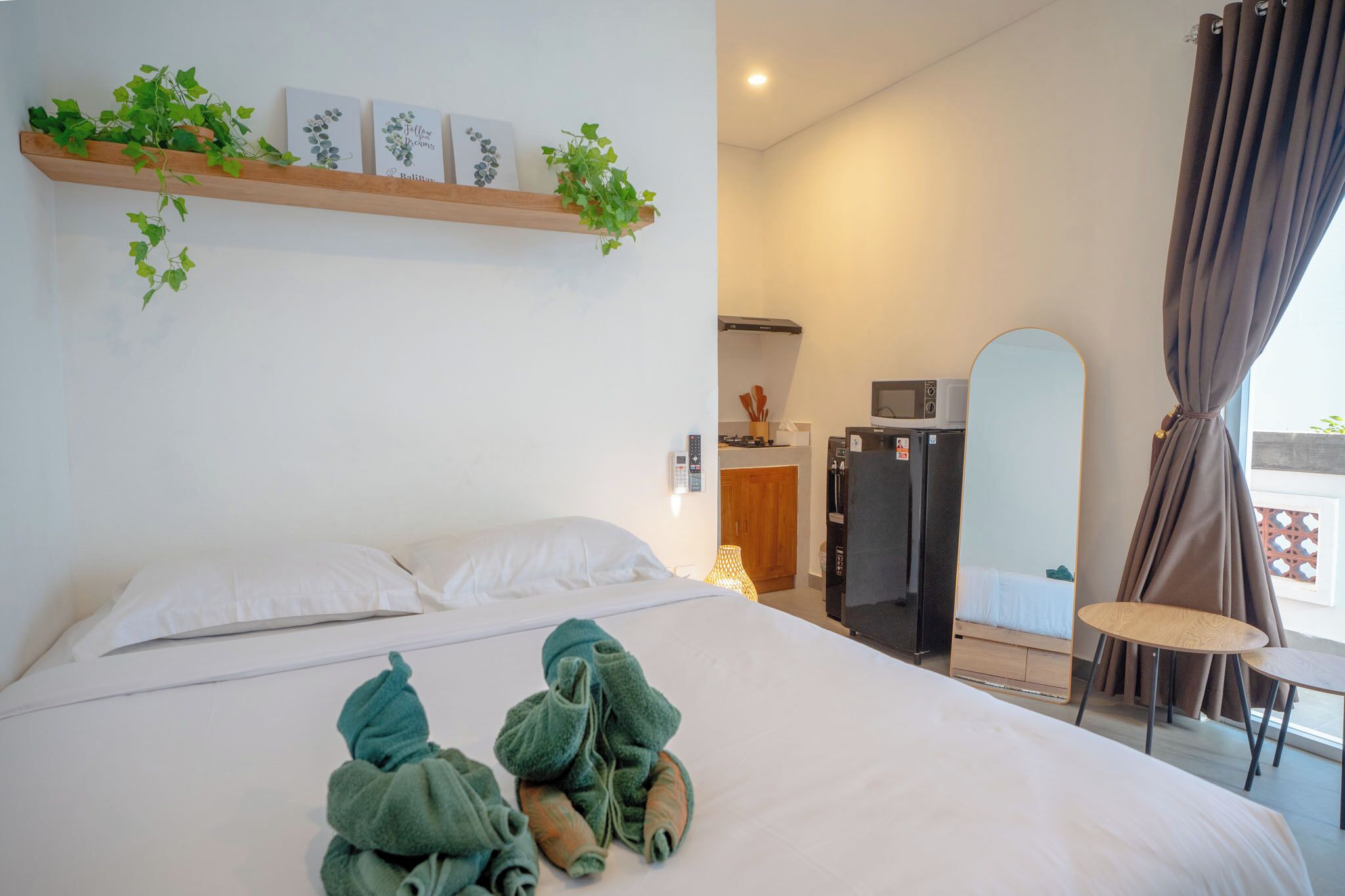 Habitación de hotel con cama, una mesita, una silla, microondas, refrigerador y ventana con cortinas.