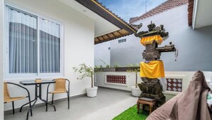 A patio with a table and chairs, a small statue, and a green artificial turf area. - Bali Bay By Urban Haven (Denpasar)