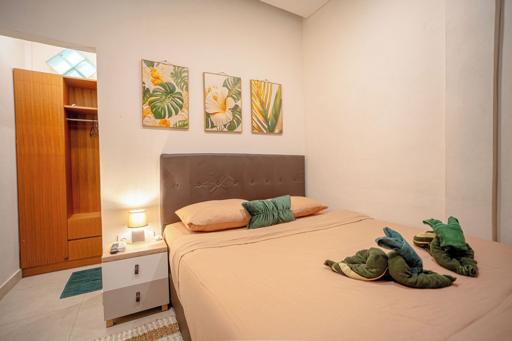 A bedroom with a bed, a nightstand, a wardrobe, and three wall-mounted paintings.