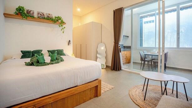 A modern bedroom with a large bed, a small table, and a view of the city through a sliding glass door. - Bali Bay By Urban Haven (Denpasar)