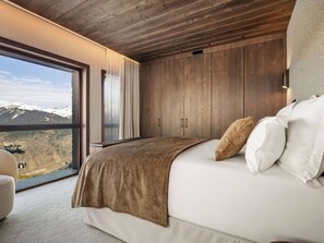 A bedroom with a large window, wooden ceiling, and a bed with white and brown bedding. - Luxury apartment with 2 suites, 6 sleeps, indoor pool at Courchevel 1850 (Courchevel 1850)