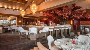 A restaurant with a bar area, white fur-covered chairs, and a marble table set for dining.
