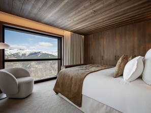A bedroom with a large window, a bed, a chair, and wooden walls.