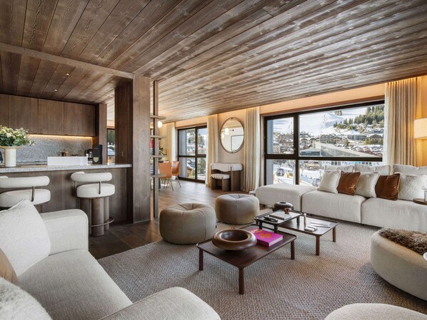 A modern living room with a kitchen area, large windows, and a view of the city.