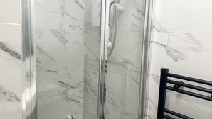 A glass-enclosed shower with a handheld showerhead and a wall-mounted faucet.
