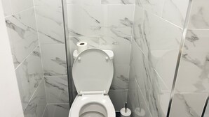 A bathroom with a toilet, marble tiles, and a roll of toilet paper on the wall.