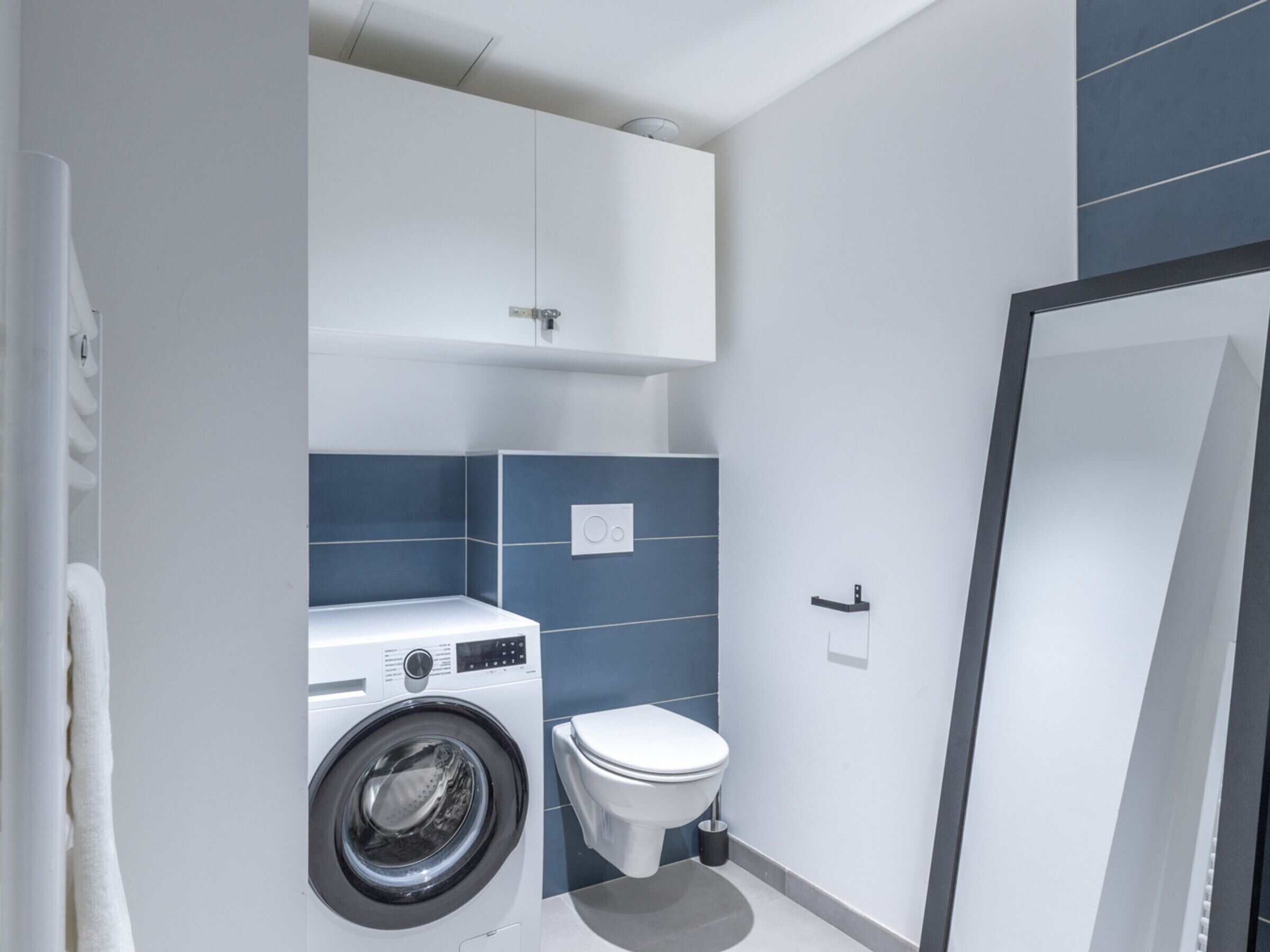 Une petite salle de bain équipée d’un lave-linge, de toilettes et d’un porte-serviettes.