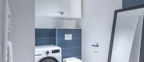 Une petite salle de bain équipée d’un lave-linge, de toilettes et d’un porte-serviettes.