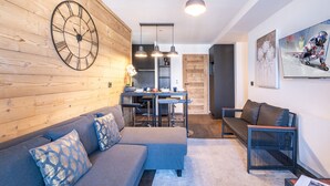 Una sala de estar moderna con una pared de madera, un reloj grande, un sofá, una mesa de centro y un comedor con una mesa y sillas.