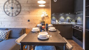 Una cocina moderna con armarios oscuros, un reloj de pared de madera y un comedor con una mesa dispuesta para cuatro.