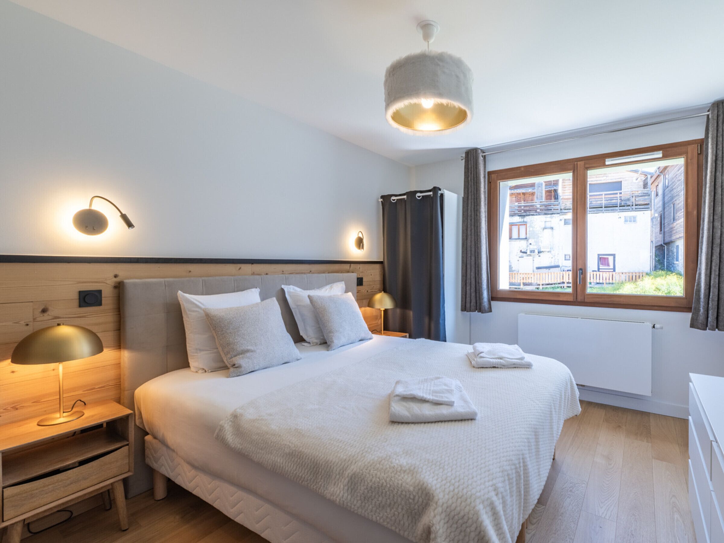 A modern bedroom with a large bed, bedside lamps, a view of the outside, and a window with curtains.