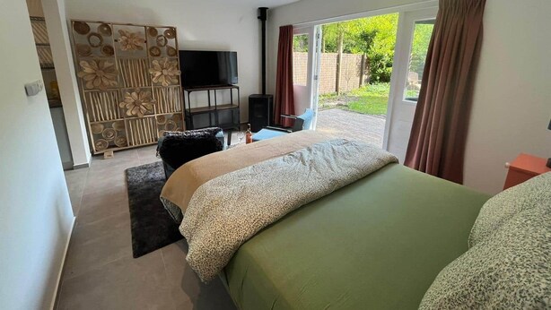 Un dormitorio con cama, televisor, escritorio y vistas al exterior.