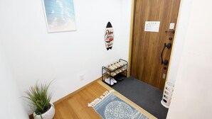 Un pasillo con una puerta de madera, un zapatero, un cuadro enmarco y una planta en maceta.