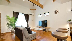 Una sala de estar moderna con un sofá gris, un televisor, piso de madera y un amplio ventanal con cortinas.