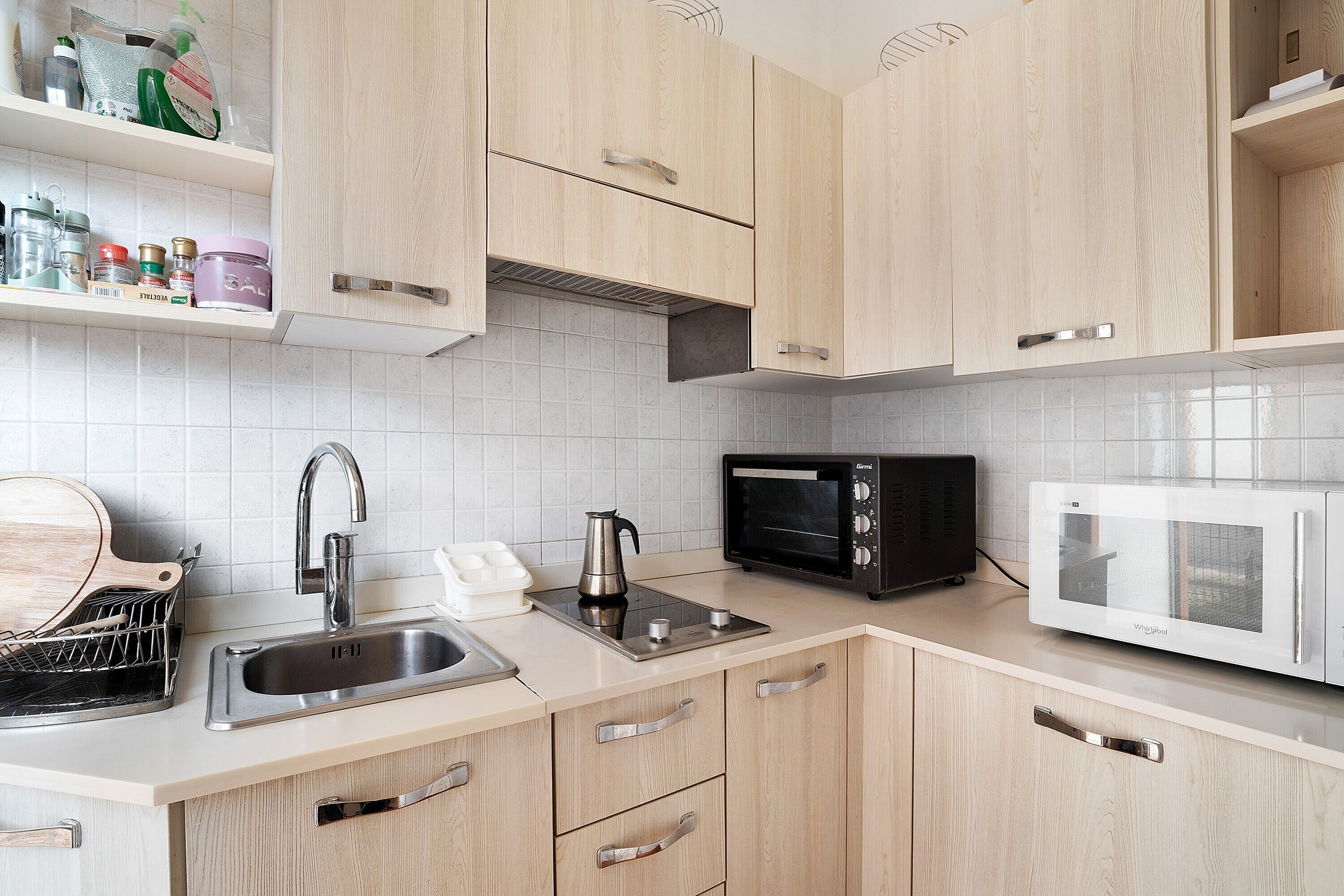 A kitchen with wooden cabinets, a stainless steel sink, a kettle, a toaster oven, and a microwave.