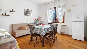 A dining area with a table set for four, a sofa, a refrigerator, and a window with curtains.