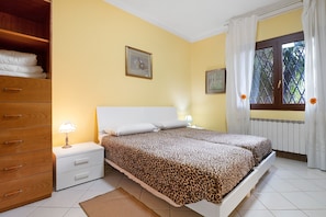 A bedroom with two beds, a wooden dresser, a nightstand with a lamp, and a window with curtains.