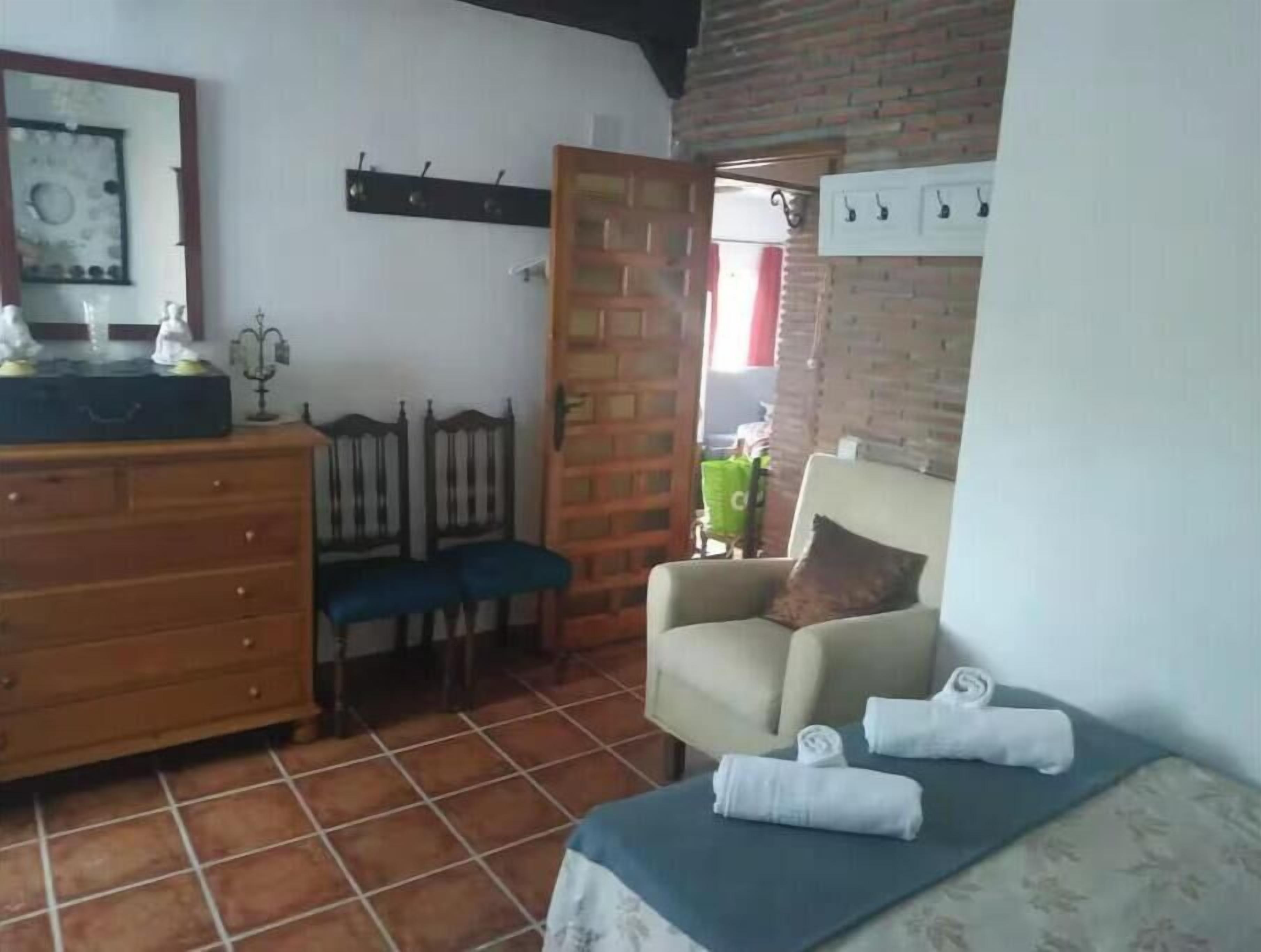 Een kleine, gezellige kamer met een houten dressoir, een blauwe stoel, een fauteuil en een tafeltje met handdoeken.