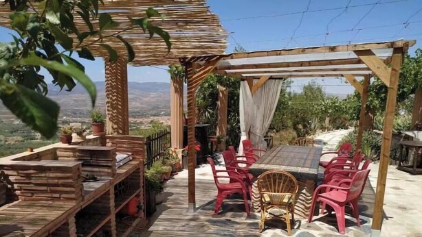 An outdoor patio with a wooden pergola, red plastic chairs, a table, and potted plants. - Loma Negra Rural House, with fireplace, swimming pool and barbecue (Dúrcal)
