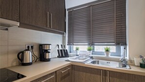 A modern kitchen with dark wooden cabinets, a stainless steel sink, a kettle, a coffee maker, and a window with blinds.