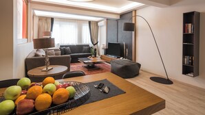 A modern living room with a sofa, a coffee table, a flat-screen TV, a bookshelf, and a fruit basket.