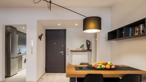A modern kitchen with a built-in refrigerator and washing machine, a dining area with a wooden table and black chairs, and a bookshelf with books.