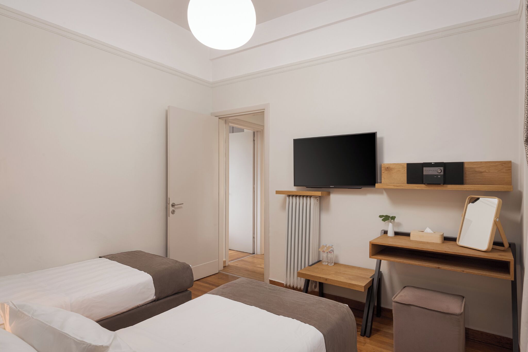 Ein Hotelzimmer mit zwei Betten, einem Fernseher, einem Schreibtisch mit Spiegel und einem Heizkörper.