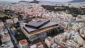 Un bâtiment moderne doté d’un toit plat et de grandes fenêtres, entouré d’un quartier urbain densément peuplé, avec divers immeubles et une montagne en arrière-plan.
