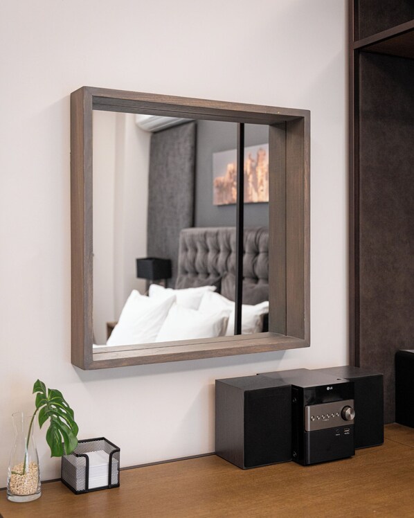 A modern living room with a large mirror, a grey tufted sofa, a black entertainment unit, and a small plant on the floor.