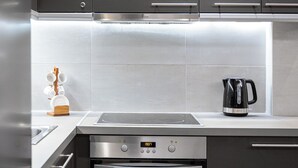 Une cuisine moderne avec des meubles de couleur sombre, une hotte en acier inoxydable, une bouilloire et un four encastré.